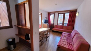 En kompakt opholdsstue med tekøkken, spiseplads og siddeområde med sofa og TV.