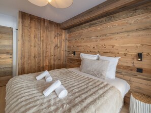 A bedroom with a wooden wall panel, a bed with white linens, and a fluffy beige blanket. - Elegant apartment at the foot of the slopes, Alpe d'Huez (Huez)