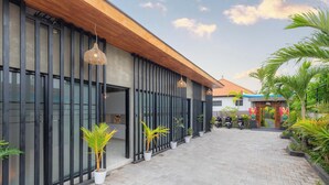 A modern building with large windows, a wooden roof, and potted plants along the walkway. - Gangga Homestay Pererenan (Munggu)