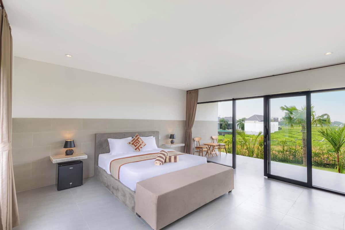 A modern bedroom with a large bed, bedside tables, a small desk, and a view of a green landscape through large windows.