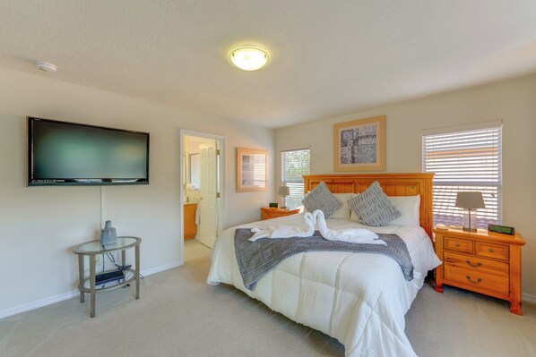 A bedroom with a bed, a TV mounted on the wall, a bedside table, a lamp, and a window with blinds. - Poolside Living: Family Retreat 12 Mi to Disney (Davenport)
