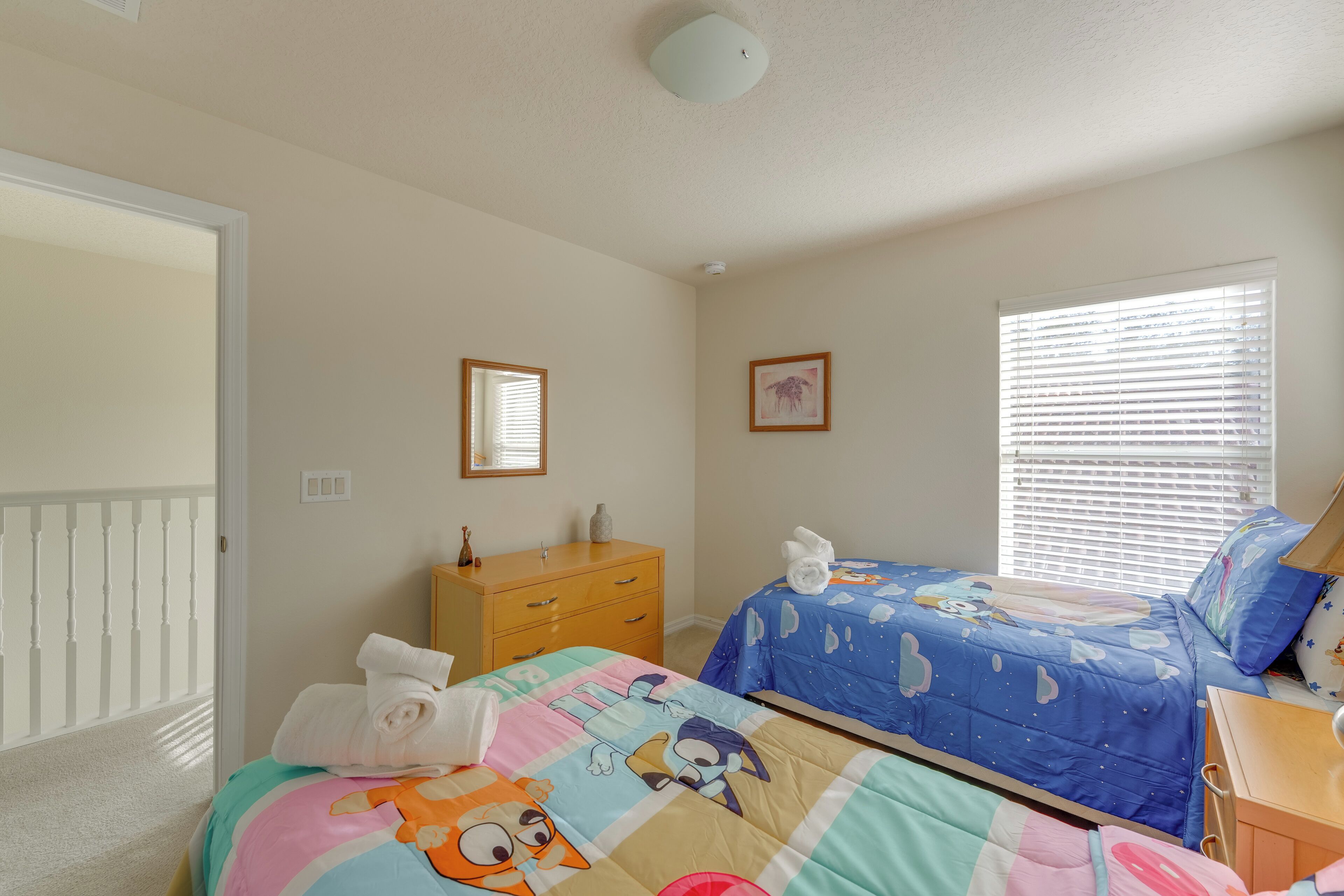 A bedroom with two beds, a dresser, and a window with blinds.