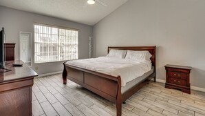 Ein Schlafzimmer mit einem hölzernen Bett, einem Nachttisch, einem Schreibtisch und einem Fenster mit Jalousien.