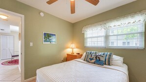 A bedroom with a bed, a nightstand, a lamp, a window with blinds, a door, and a painting on the wall. - Walk to Beach! Treasure Island Gem w/ Water Views (Treasure Island)