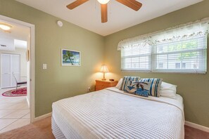 A bedroom with a bed, a nightstand, a lamp, a window with blinds, a door, and a painting on the wall. - Walk to Beach! Treasure Island Gem w/ Water Views (Treasure Island)