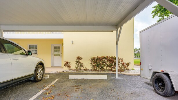 A parking area with a white car and a trailer, a building with a yellow wall and a white door, and some plants near the entrance. - Walk to Beach! Treasure Island Gem w/ Water Views (Treasure Island)