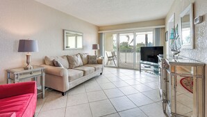 A living room with a beige sofa, a red armchair, a glass coffee table, a TV, and a decorative cabinet. - Walk to Beach! Treasure Island Gem w/ Water Views (Treasure Island)