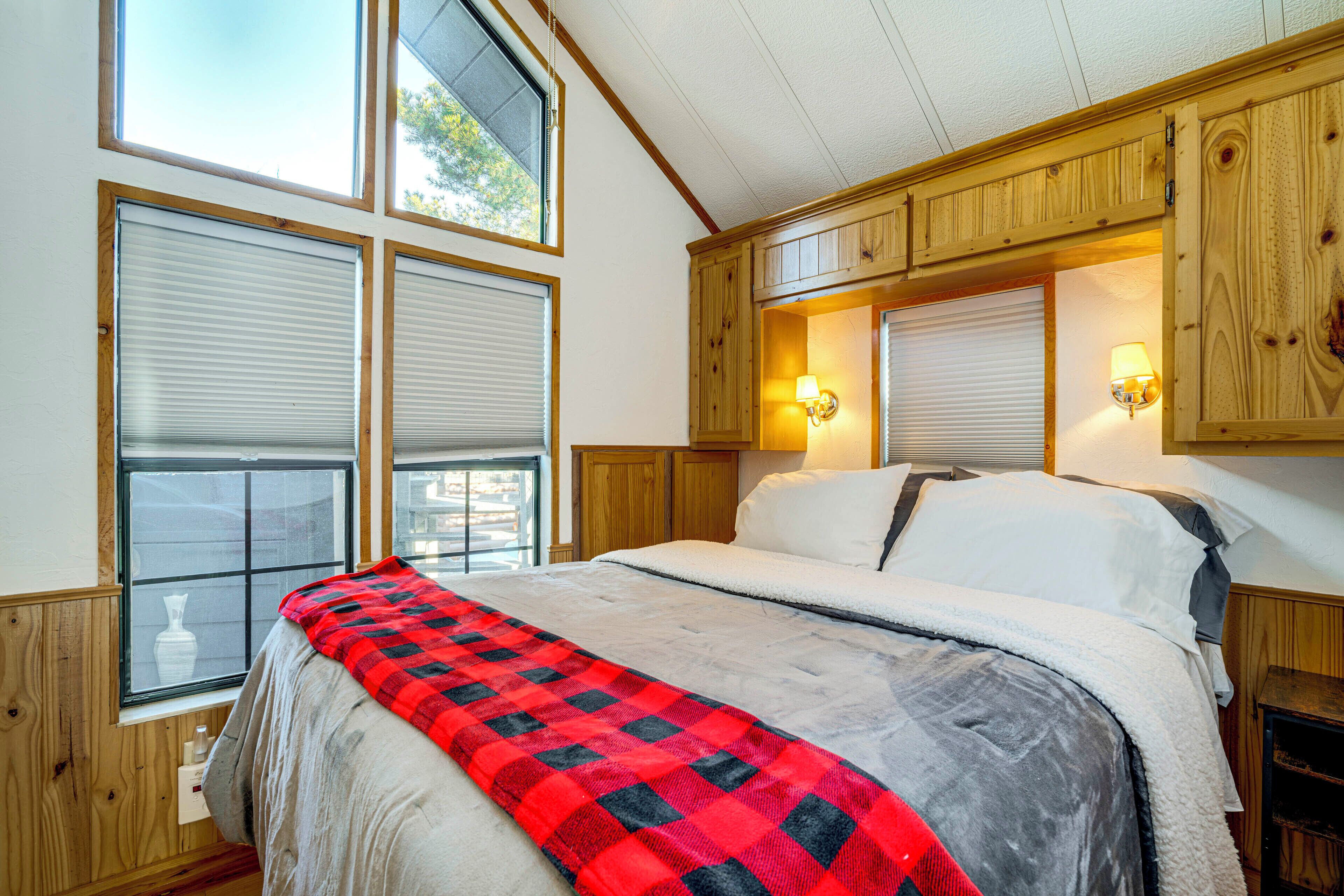 A bedroom with a large bed, wooden headboard, and two windows with blinds.