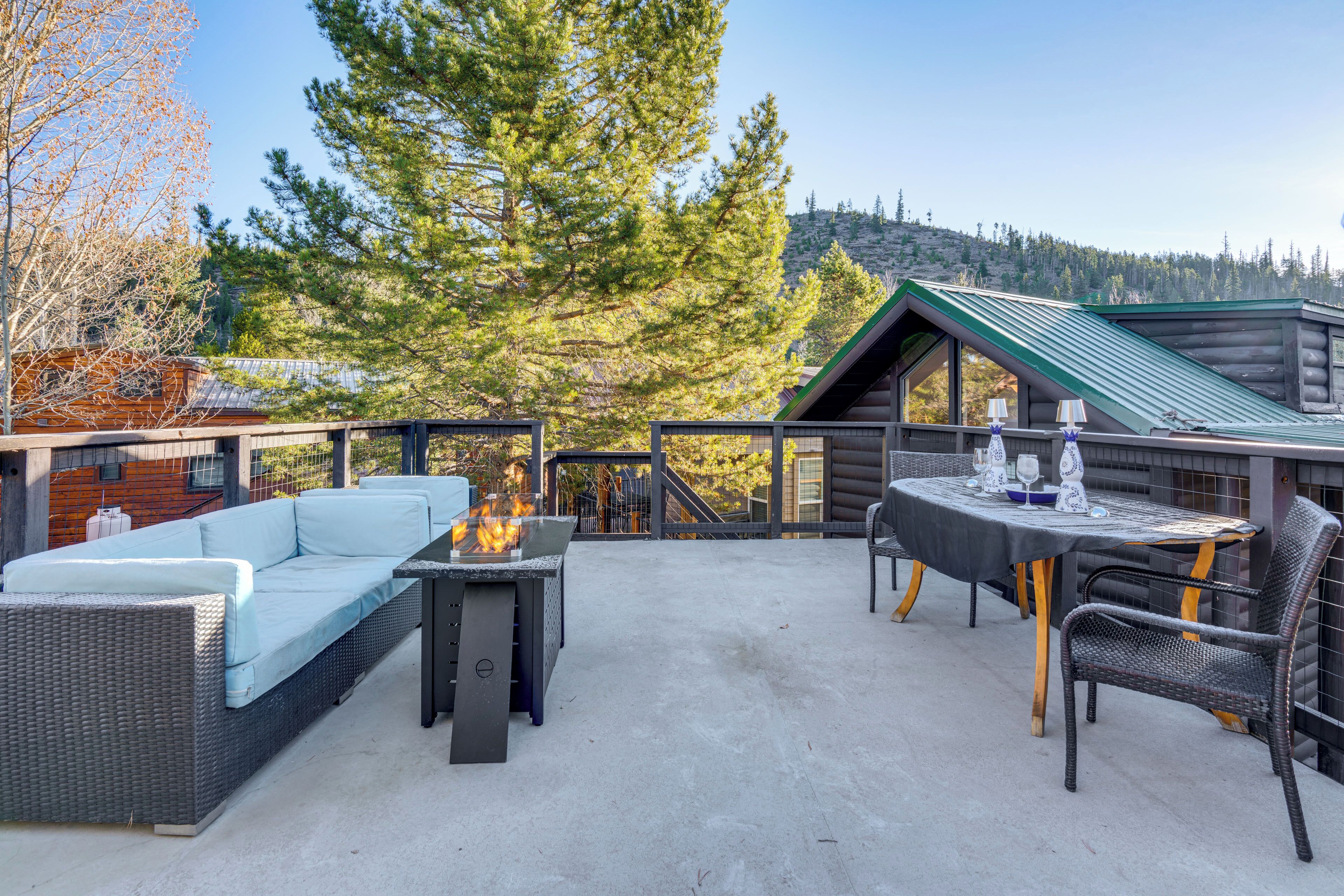 A patio with a sofa, table, and chairs, overlooking a forested area and a cabin.