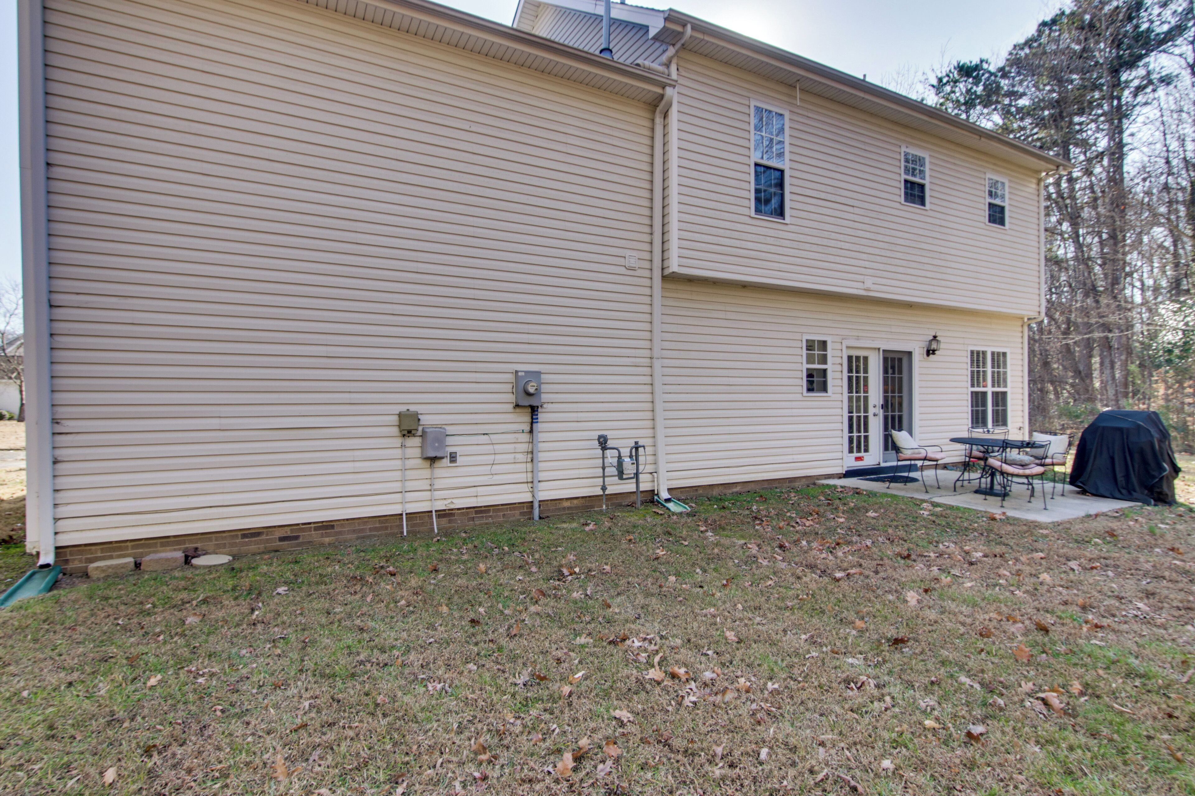 A two-story house with a covered patio, a grill, and a small outdoor seating area.