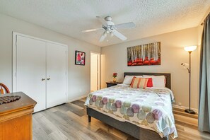 Een slaapkamer met een bed, een plafondventilator, een schilderij, een nachtkastje en een lamp.