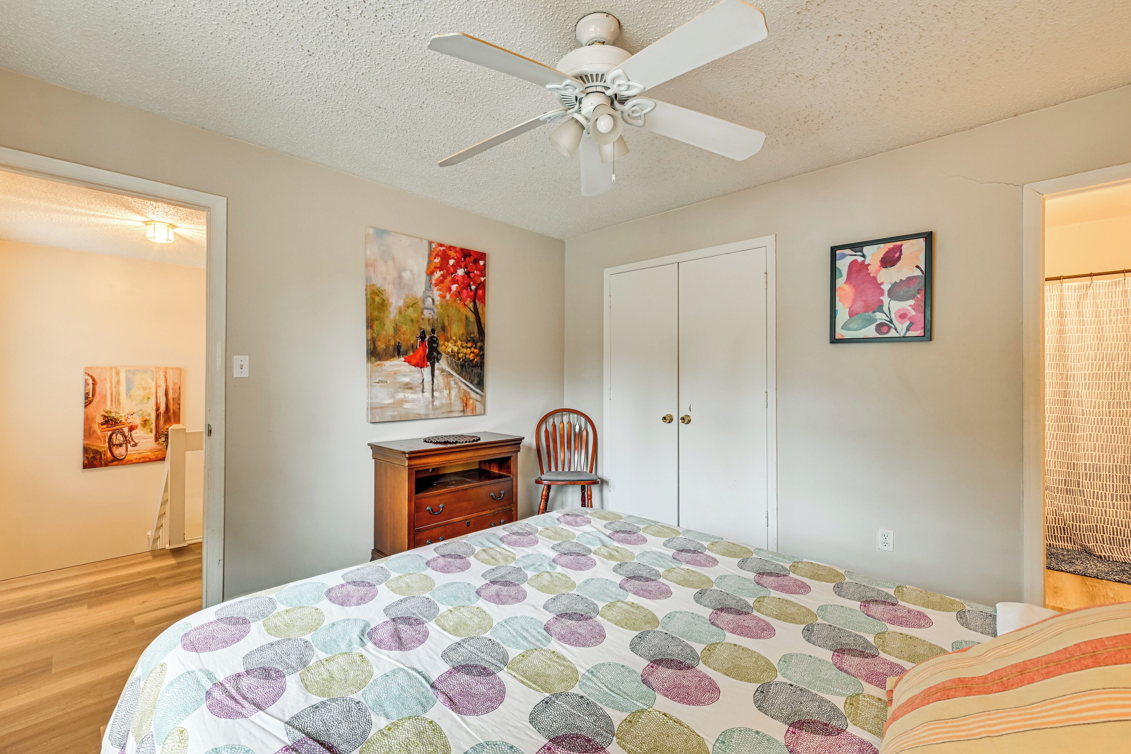 Une chambre à coucher comprenant un lit, un ventilateur de plafond, une chaise, une commode et deux portes.