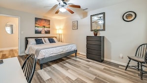 Une chambre à coucher comprenant un lit, une commode, une chaise, un ventilateur de plafond et un tableau accroché au mur.