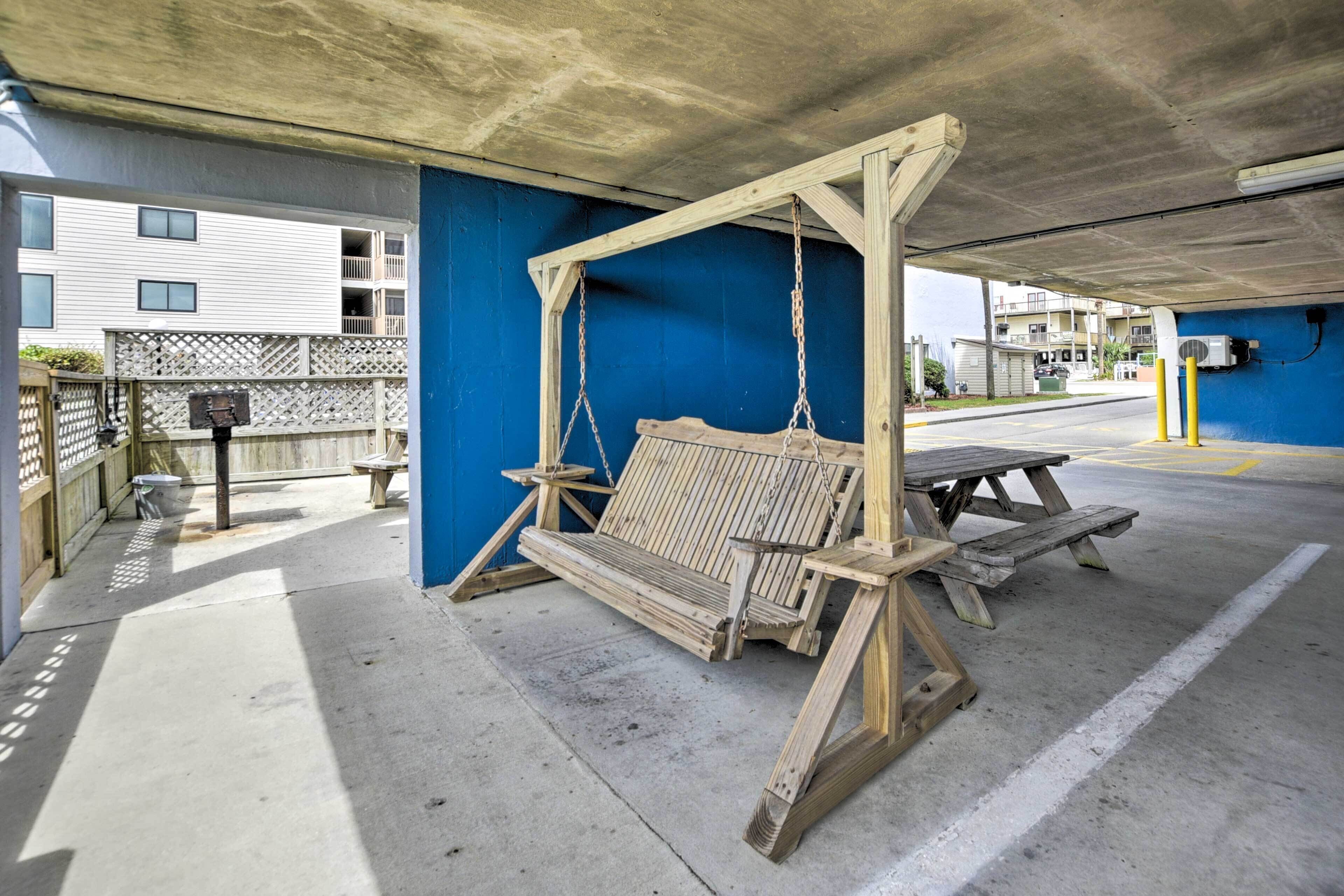 Un espace extérieur abrité, doté d’une balançoire en bois, d’une table de pique-nique et d’un sol en béton.