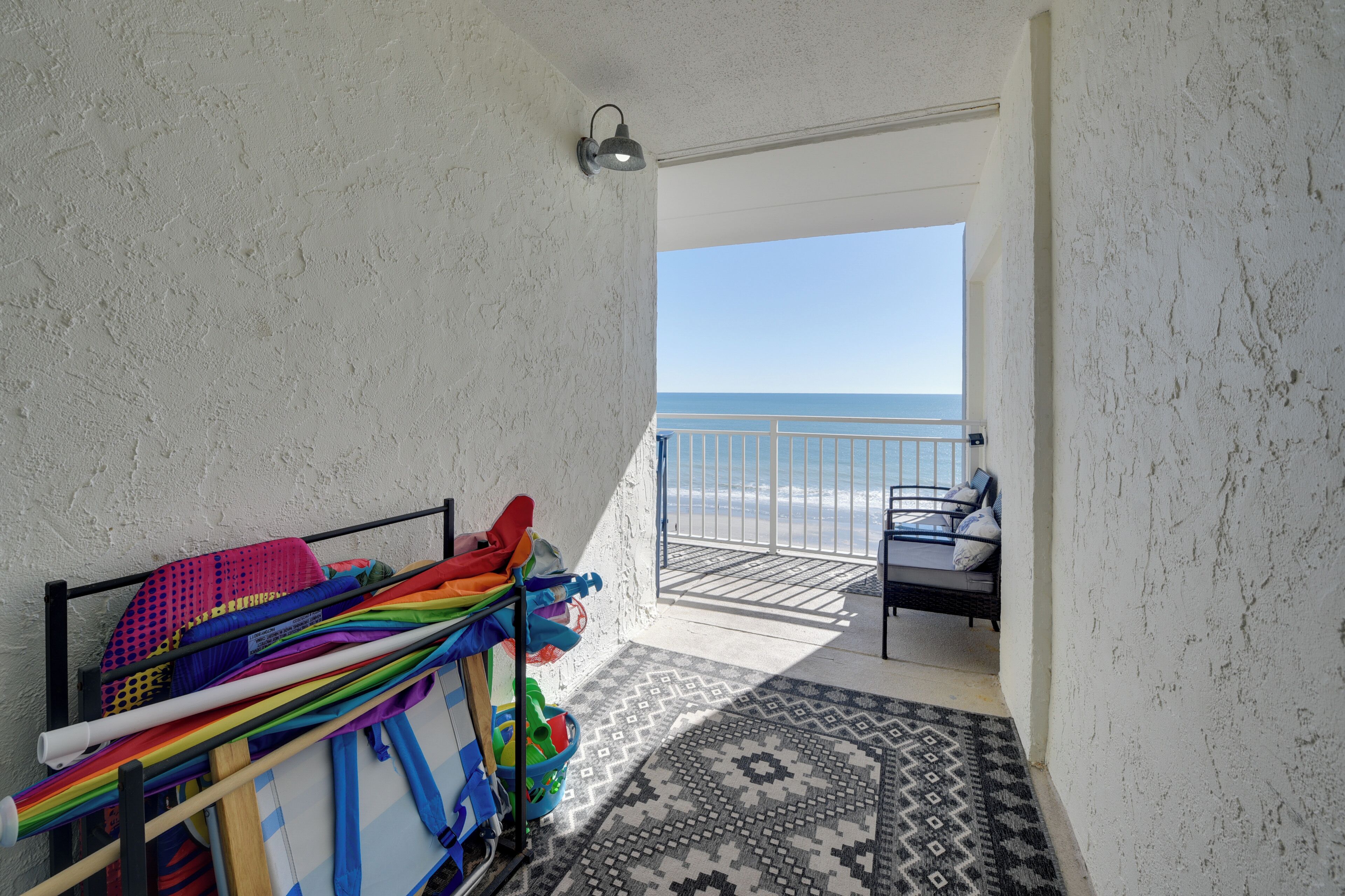 Un balcon avec vue sur l’océan, un présentoir en métal orné d’objets colorés et un tapis à motifs.
