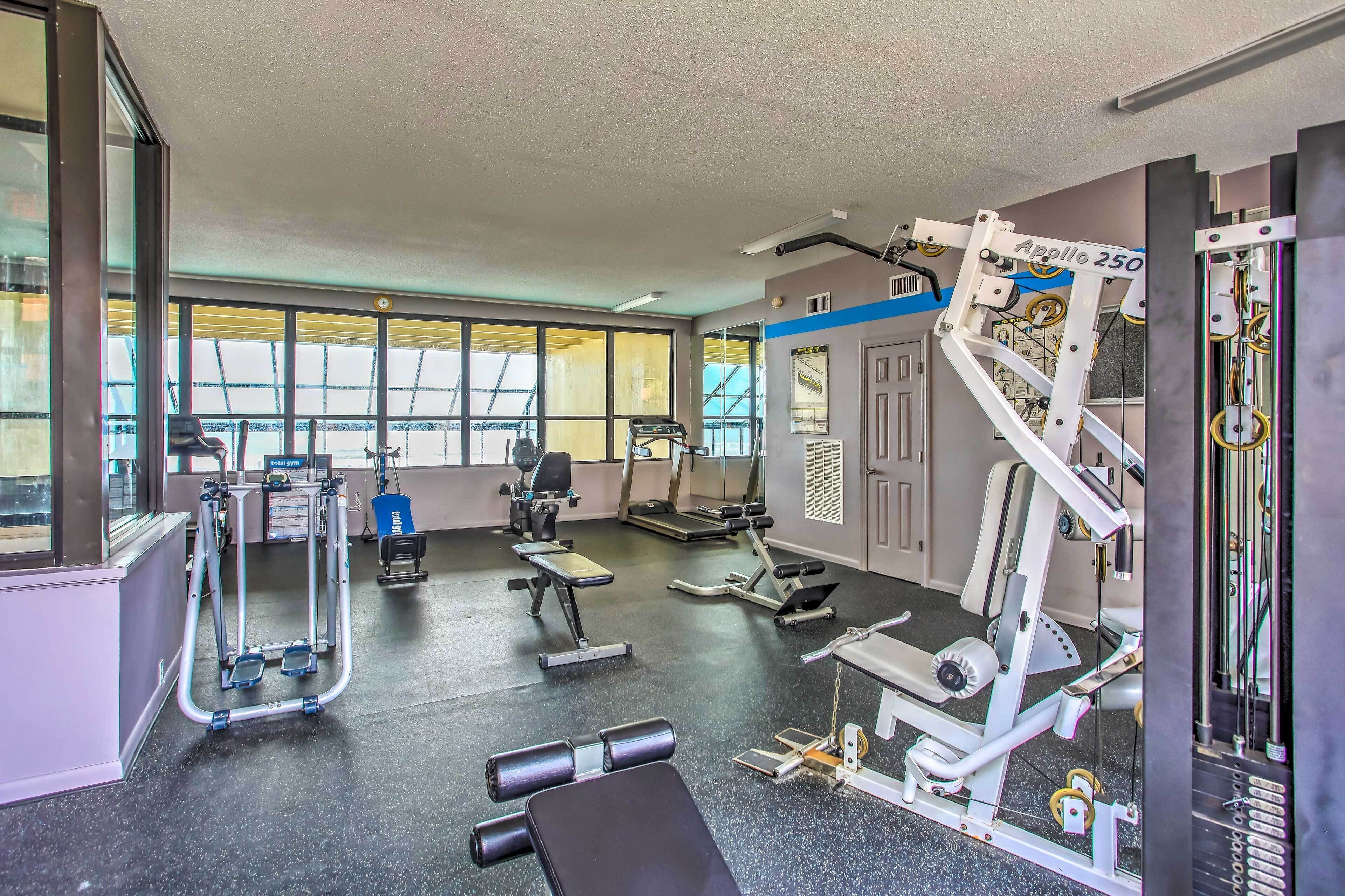 Une salle de sport équipée de divers appareils d’exercice, dotée de grandes fenêtres et d’une porte.