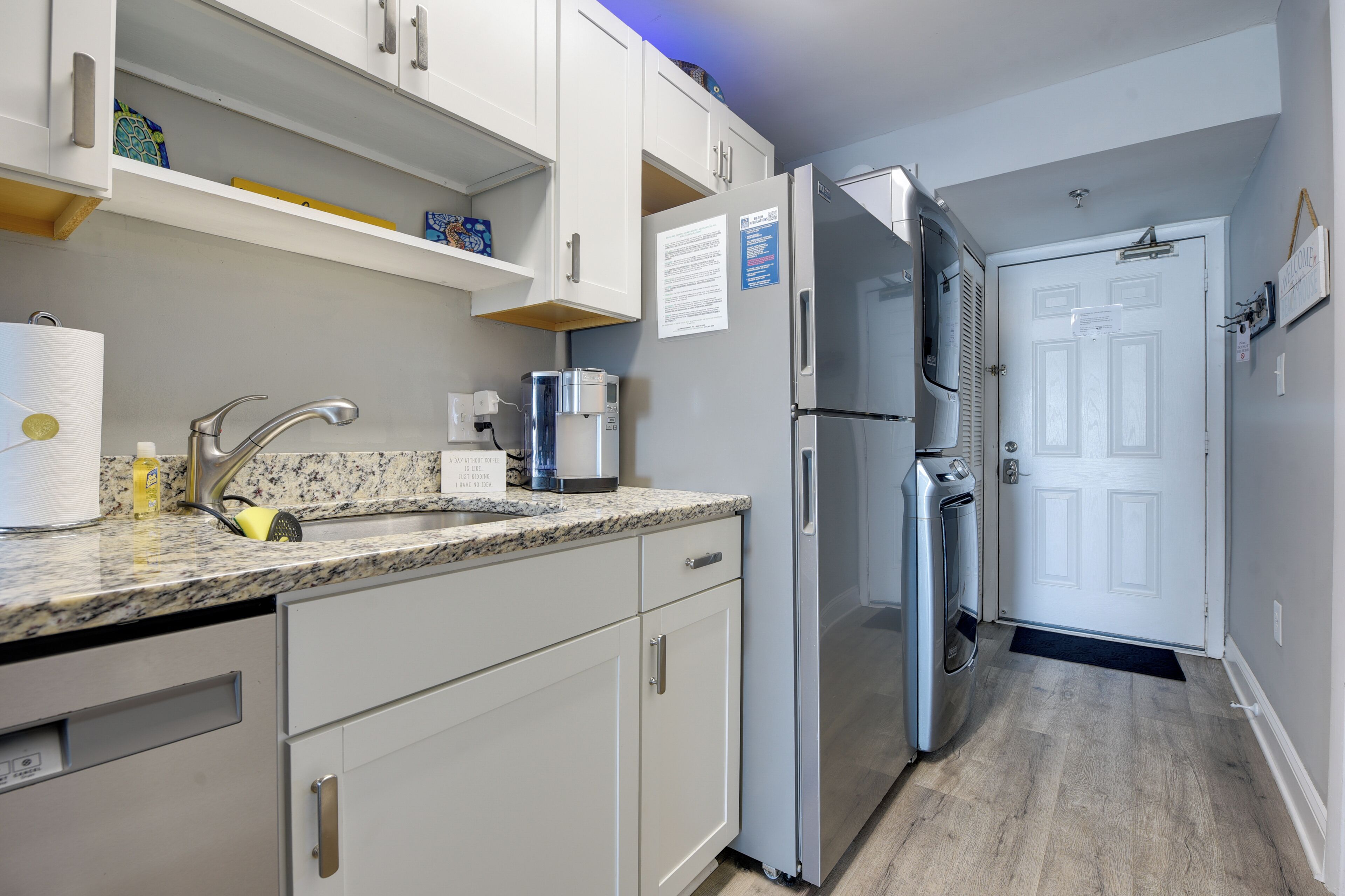 Una cocina con gabinetes blancos, encimera de granito, refrigerador de acero inoxidable y horno empotrado.