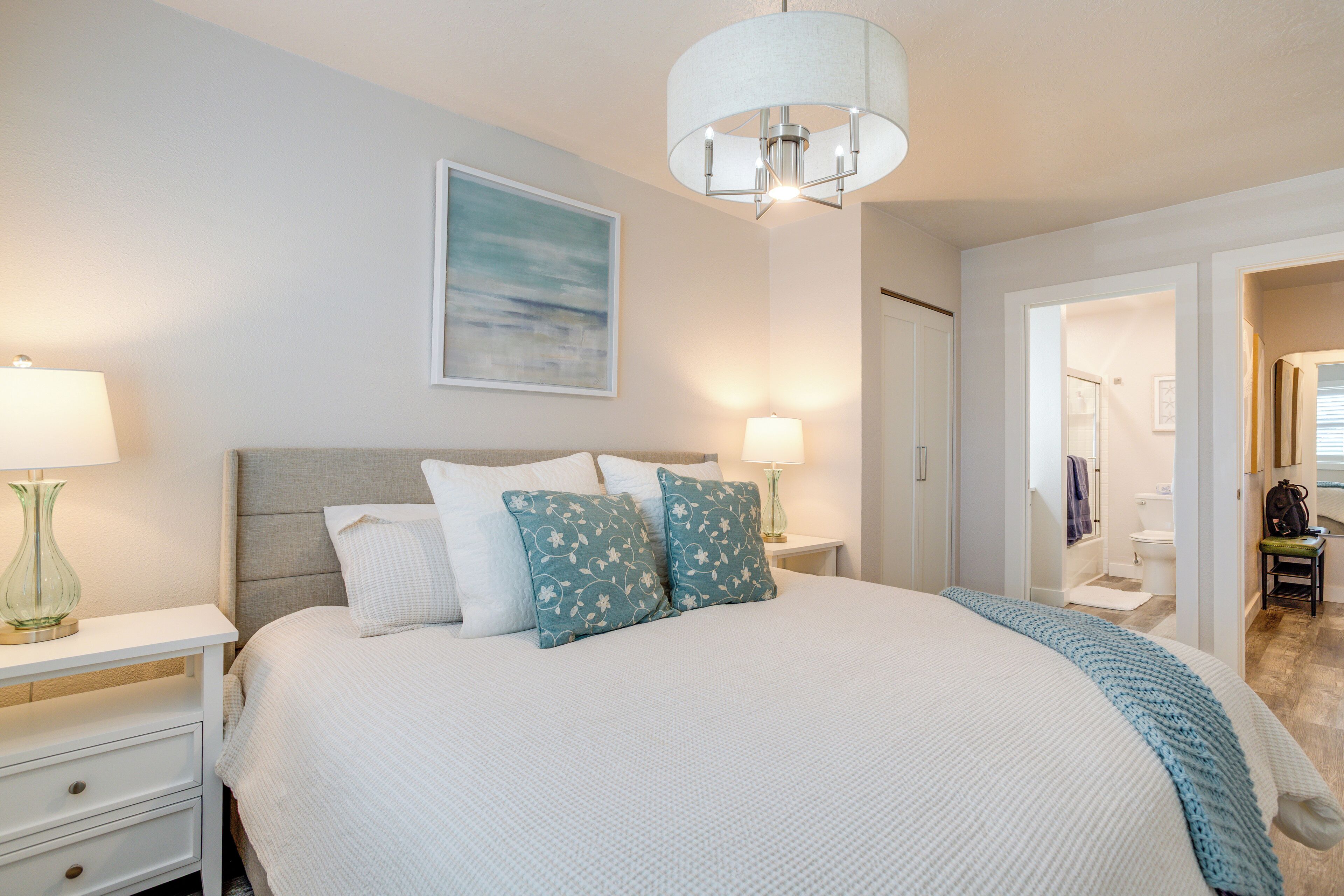 A bedroom with a large bed, two bedside tables, a nightstand, a ceiling light, and a painting on the wall.