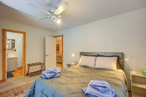 Ein Schlafzimmer mit Bett, Deckenventilator, Nachttisch, Nachttischlampe und einem durchgegangenen Türspalte sichtbaren Badezimmer.