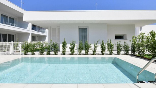 A modern building with a swimming pool, a white exterior, and a clear blue sky. - Le Jolie 1 - Carraro Immobiliare Jesolo (Jesolo)