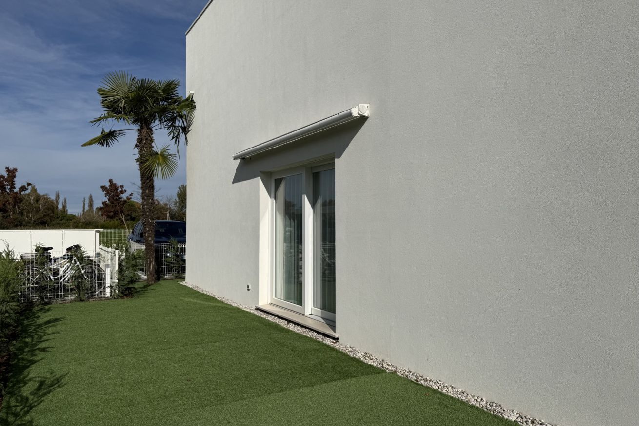 Ein modernes Gebäude mit flacher Fassade, einem kleinen Fenster mit weißem Rahmen und einem gepflegten Rasen mit einer Palme.