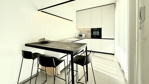 A modern kitchen with white cabinets, a dark countertop, and black chairs. - Le Jolie 1 - Carraro Immobiliare Jesolo (Jesolo)