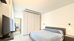 A modern bedroom with a bed, bedside table, TV, and wardrobe. - Le Jolie 1 - Carraro Immobiliare Jesolo (Jesolo)