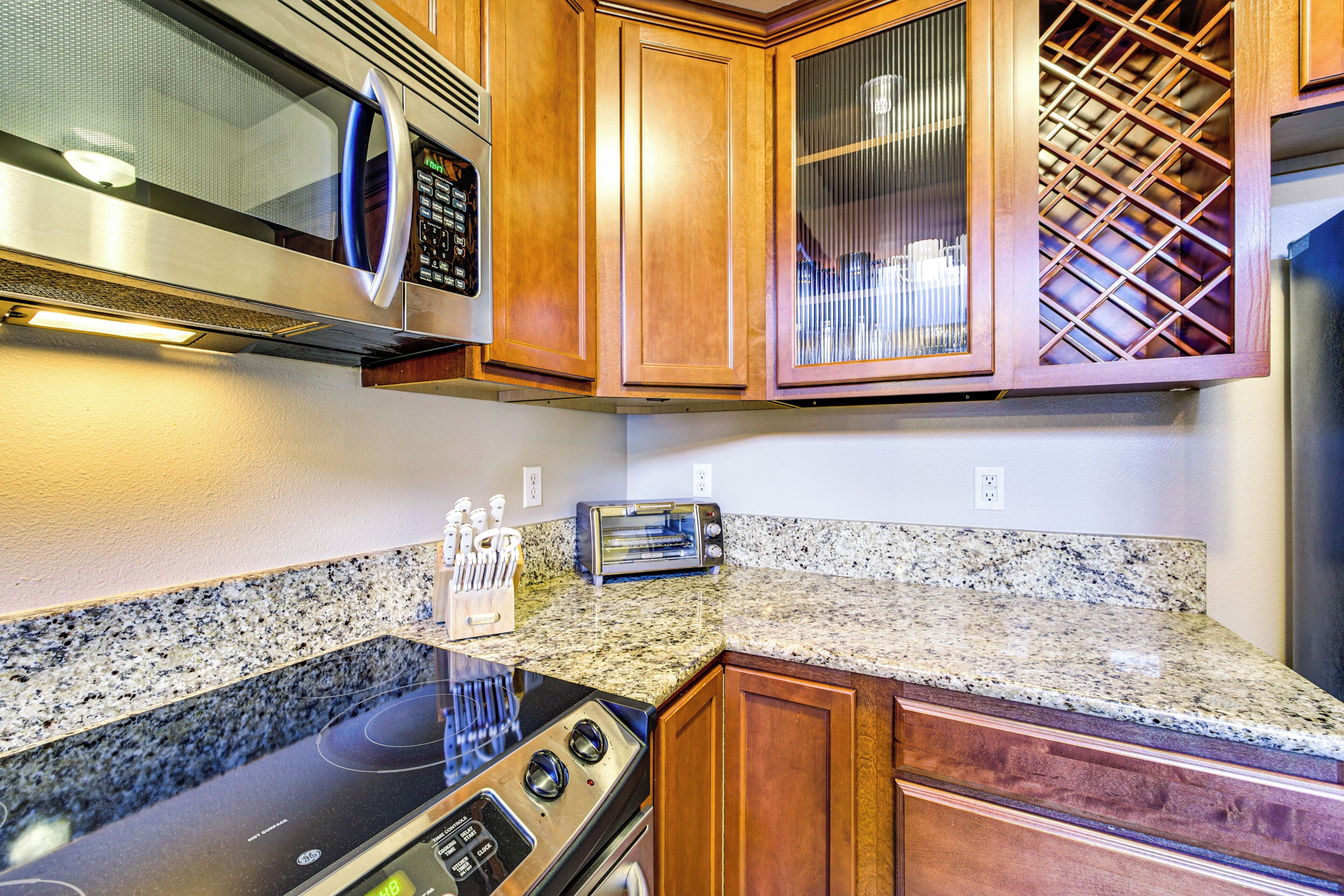A kitchen with granite countertops, wooden cabinets, a microwave, a toaster, and a stainless steel range hood.