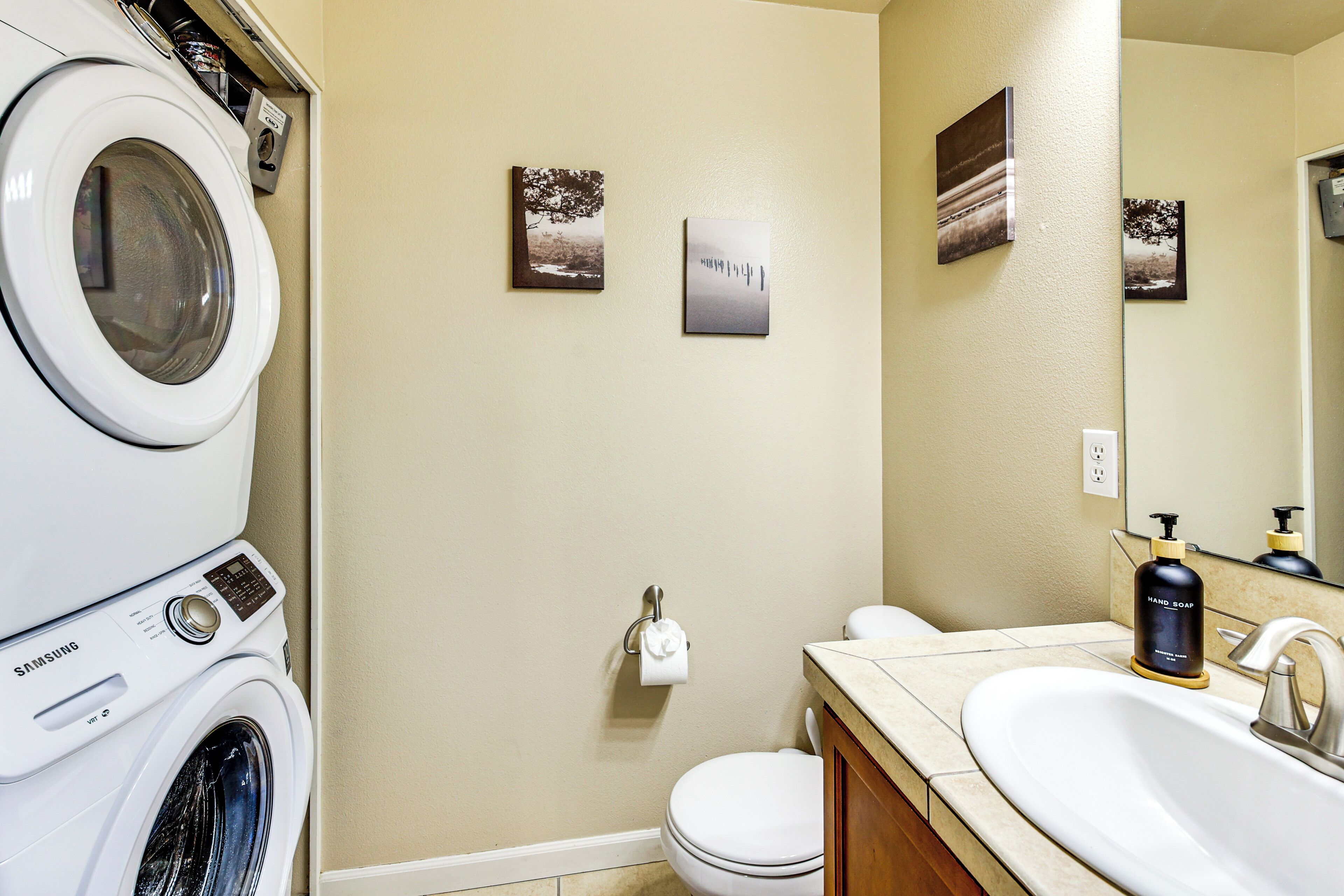 A laundry area with a Samsung washer and dryer, a toilet, and a sink with a hand soap dispenser.