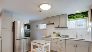 A modern kitchen with stainless steel appliances, white cabinetry, a small table, and a window with a green plant. - Work & Play Near Old Town Arvada: Pets Welcome! (Arvada)