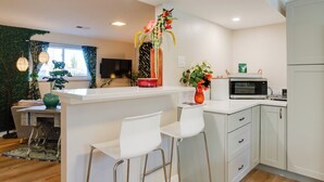 A modern kitchen with white cabinetry, a central island with bar stools, a microwave, and a decorative vase with flowers. - Work & Play Near Old Town Arvada: Pets Welcome! (Arvada)