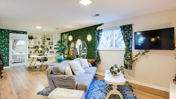 A living room with a grey sofa, a white coffee table, and a blue patterned rug. There is a television mounted on the wall and a window with curtains. - Work & Play Near Old Town Arvada: Pets Welcome! (Arvada)