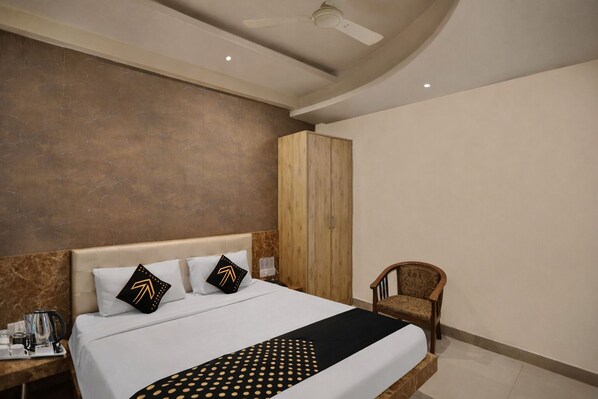 Una camera d'hotel con un letto, un armadio in legno, una sedia e un comodino con bollitore e tazze.
