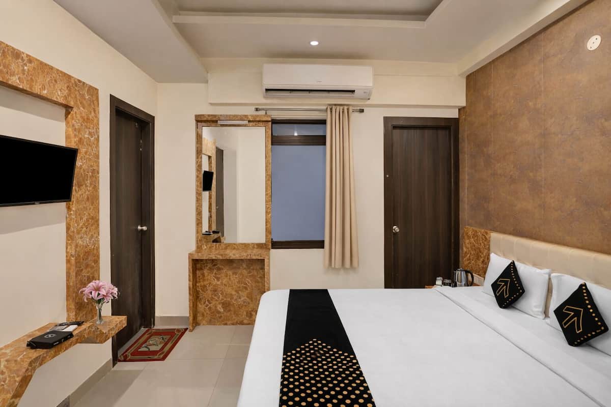 A hotel room with a bed, a TV, an air conditioning unit, a mirror, and a small table with a vase.