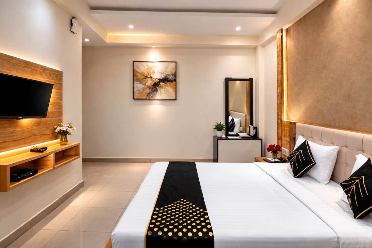 A modern hotel room with a flat-screen TV, a large bed with black and white bedding, a wooden console table, and a large mirror.