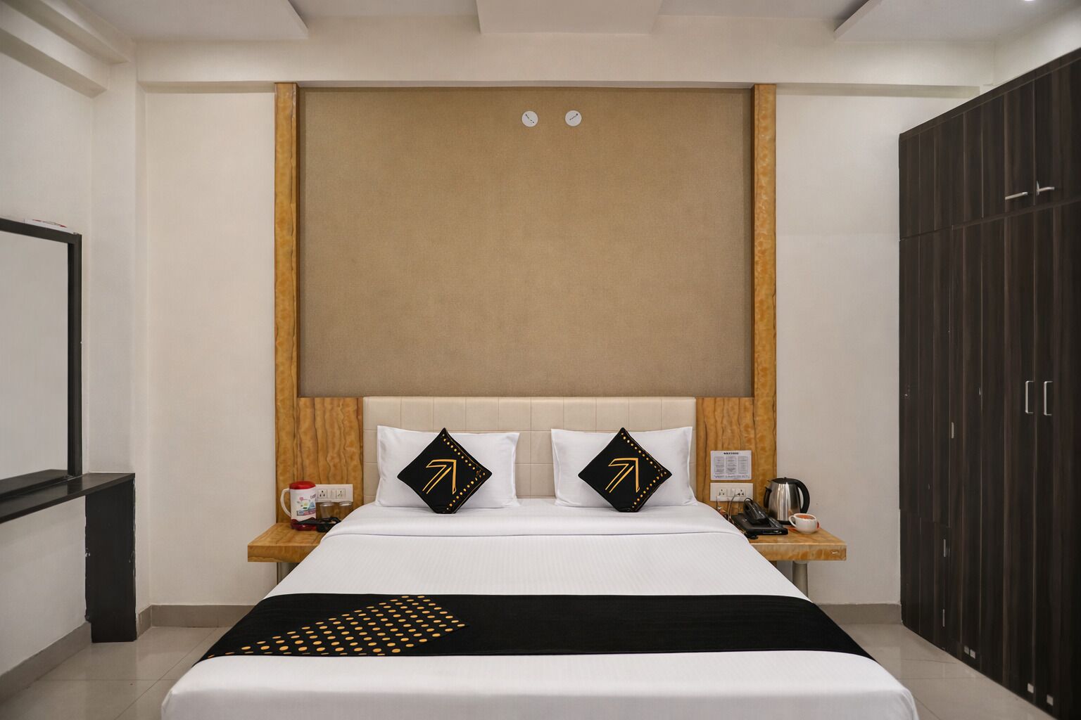A hotel room with a bed, two bedside tables, a wardrobe, and a clock on the wall.
