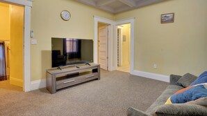 Un soggiorno con televisione a schermo piatto su un supporto in legno, tappeto beige e divano grigio con una coperta.