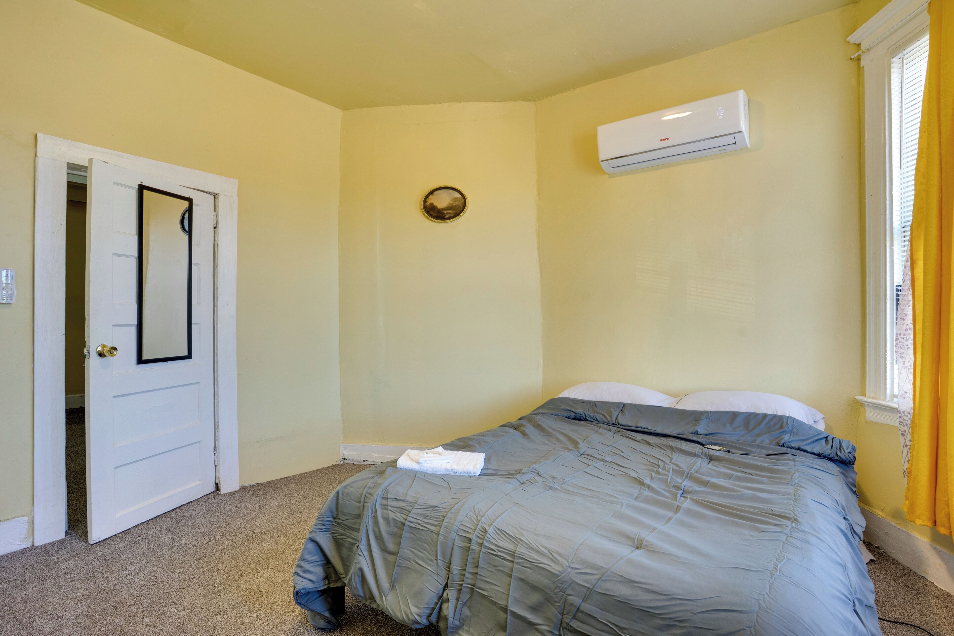 A bedroom with a bed, a door, an air conditioning unit, and a window with curtains.
