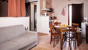 Ein Wohnzimmer mit einer Couch, ein Essbereich mit Tisch und Stühlen sowie eine Küche mit Kühlschrank.