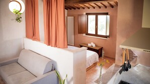 Ein gemütliches Zimmer mit einer Couch, einem kleinen Tisch mit einem Handtuch, einem Fenster mit Vorhängen, einem Heizkörper und einem Herd.