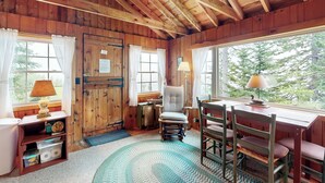 Ein gemütliches Blockhaus-Interieur mit Holzwänden, einem großen Fenster, einem Schreibtisch mit Stühlen und einer Lampe.