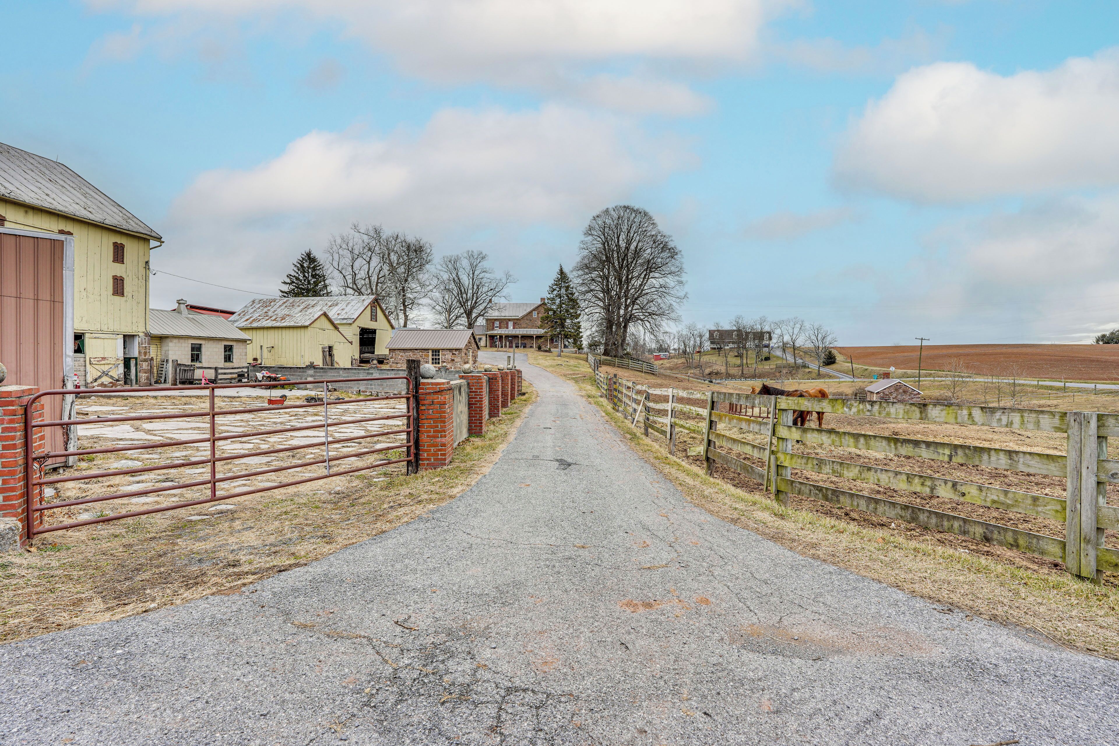 A rural road leading to a farm with barns and a fenced area.