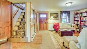 Una sala de estar acogedora con una escalera, una chimenea, una estantería y una puerta que da a otra habitación.