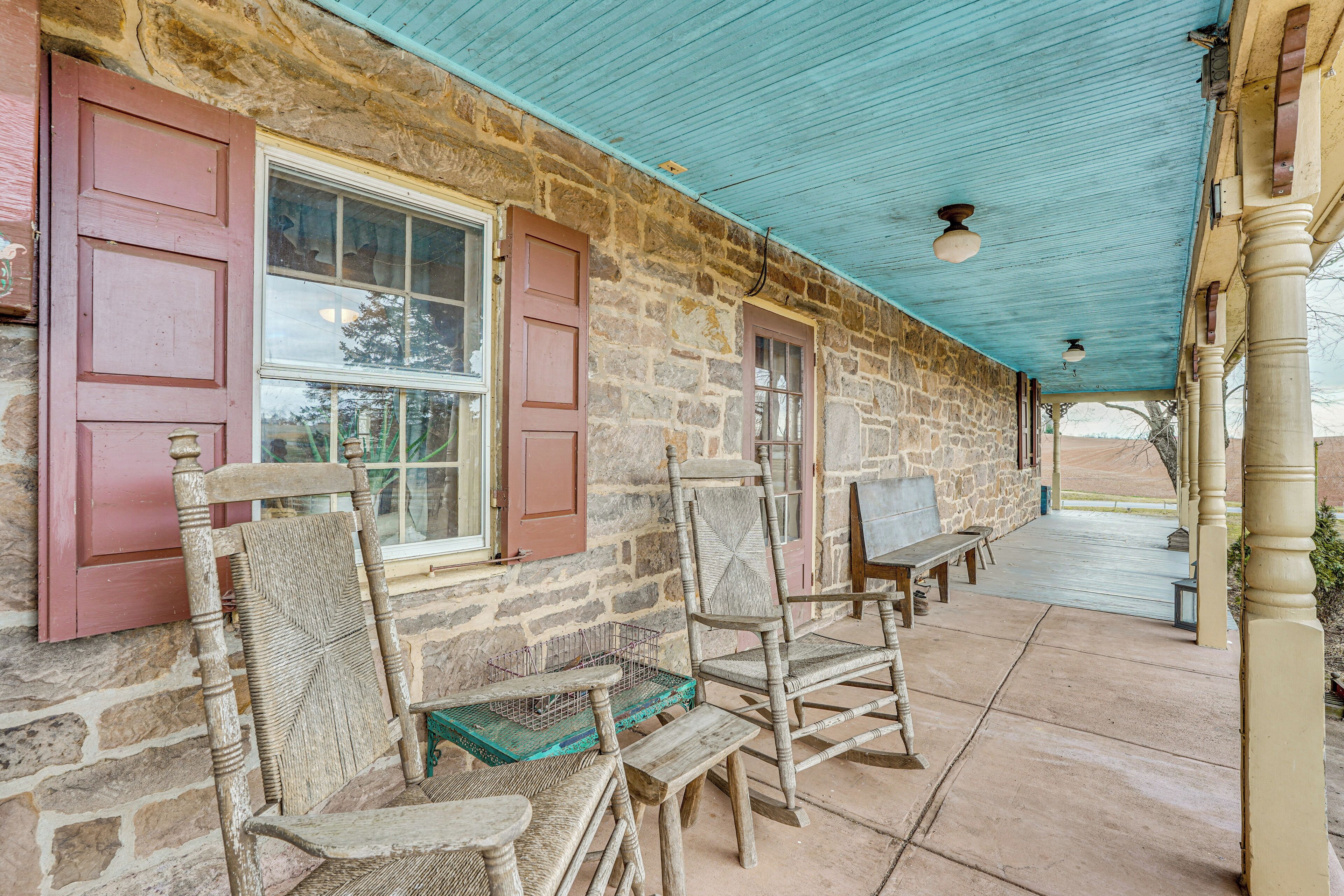 A stone building with a covered porch, wooden chairs, and a bench.