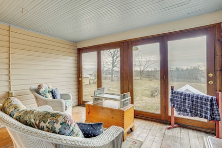 A sunroom with a wicker chair, a wooden chest, and a view through large glass doors.