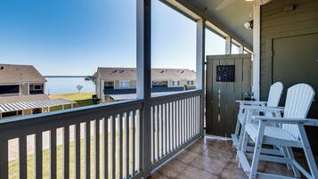 A balcony with a view of a lake, white Adirondack chairs, and a sign that says "Take Life Easy".