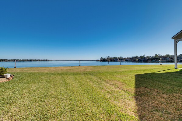 A grassy area with a view of a lake and a building in the background. - Steps to Lake Conroe! Condo w/ Balcony & Views (Montgomery)