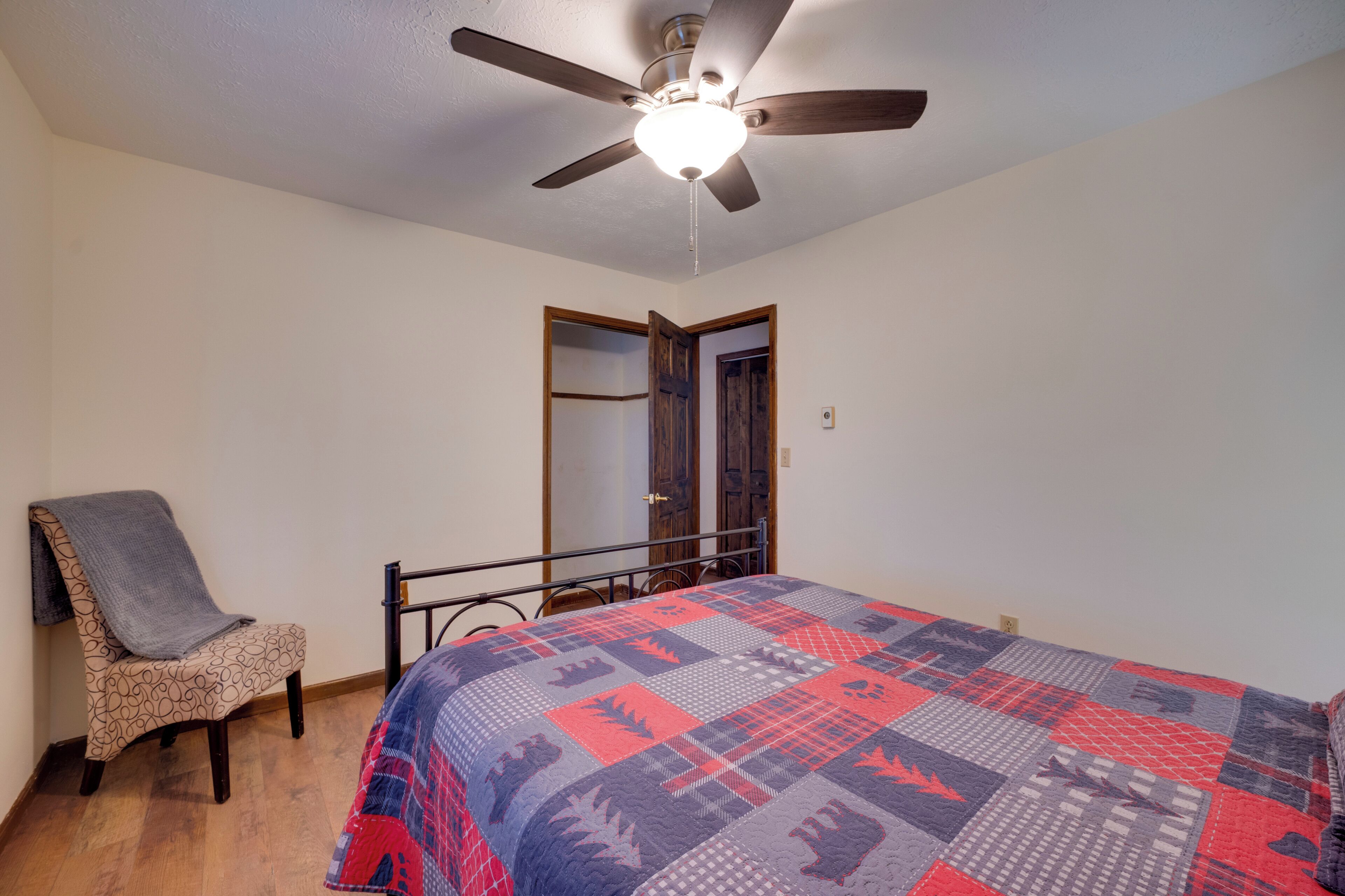 A bedroom with a bed, a chair, a ceiling fan, and a door.