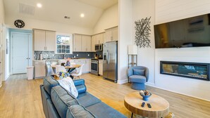 A modern kitchen with white cabinets, a stainless steel refrigerator, and a microwave. There is a dining area with a table and chairs, and a living room with a blue sofa and a fireplace. - Lake Greenwood Access: Modern Escape w/ Patio! (Greenwood)