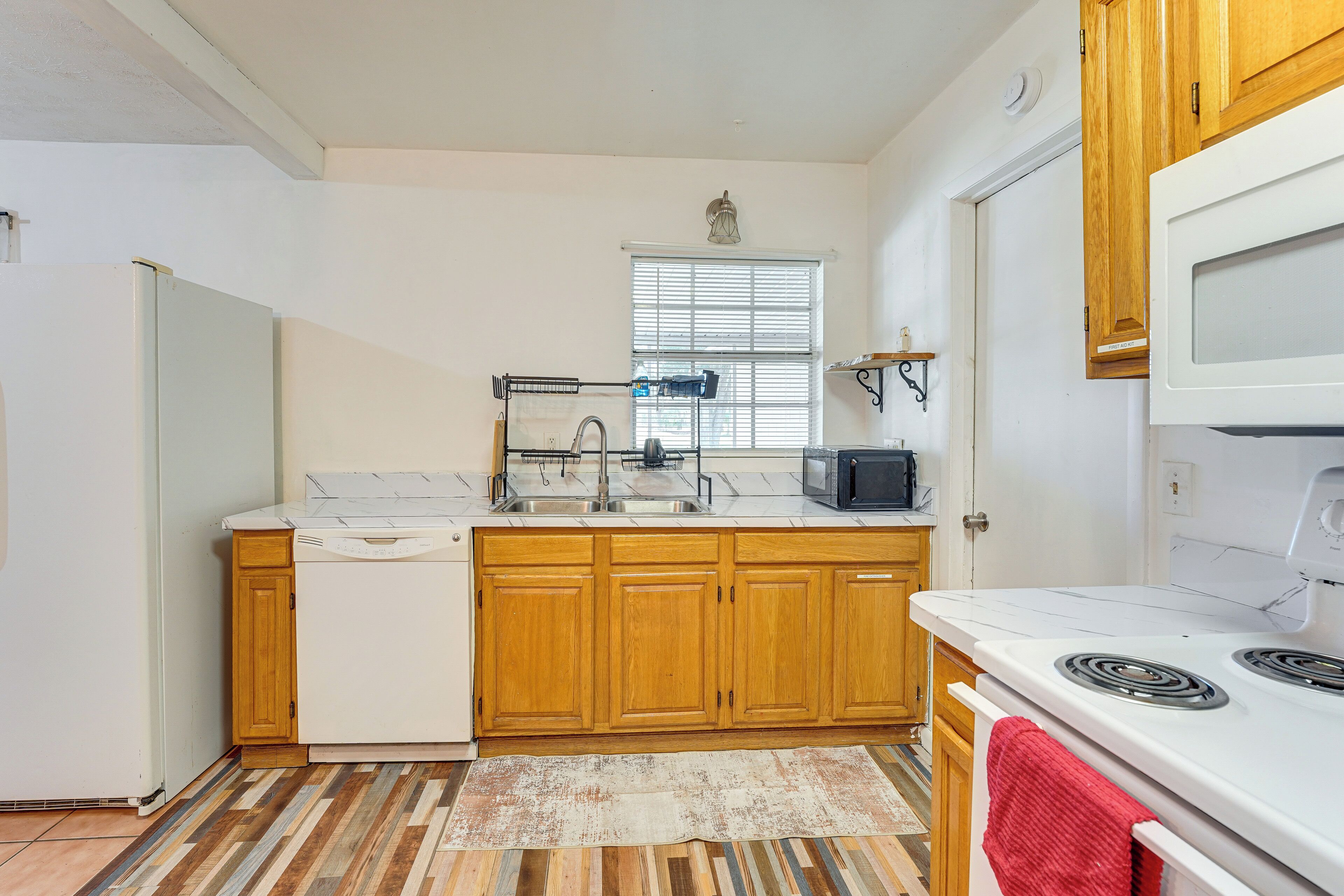 A compact kitchen with wooden cabinets, a white refrigerator, a microwave, and a stove.